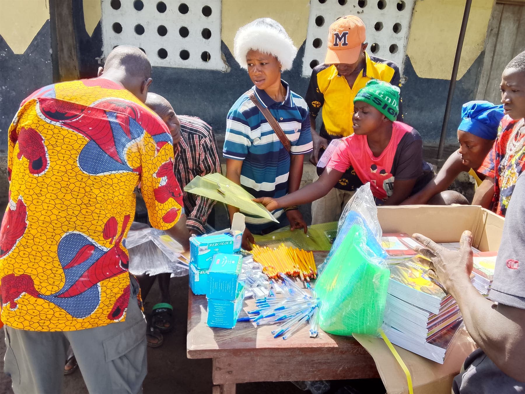 Volunteers at a table handing out pens, pencils, and exercise books to young people.