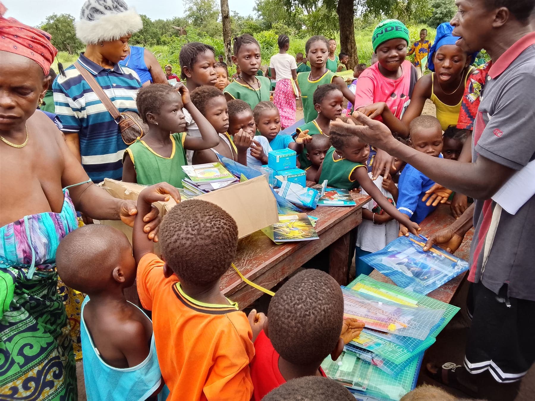Children reaching towards a table as school packs are handed out by adults.