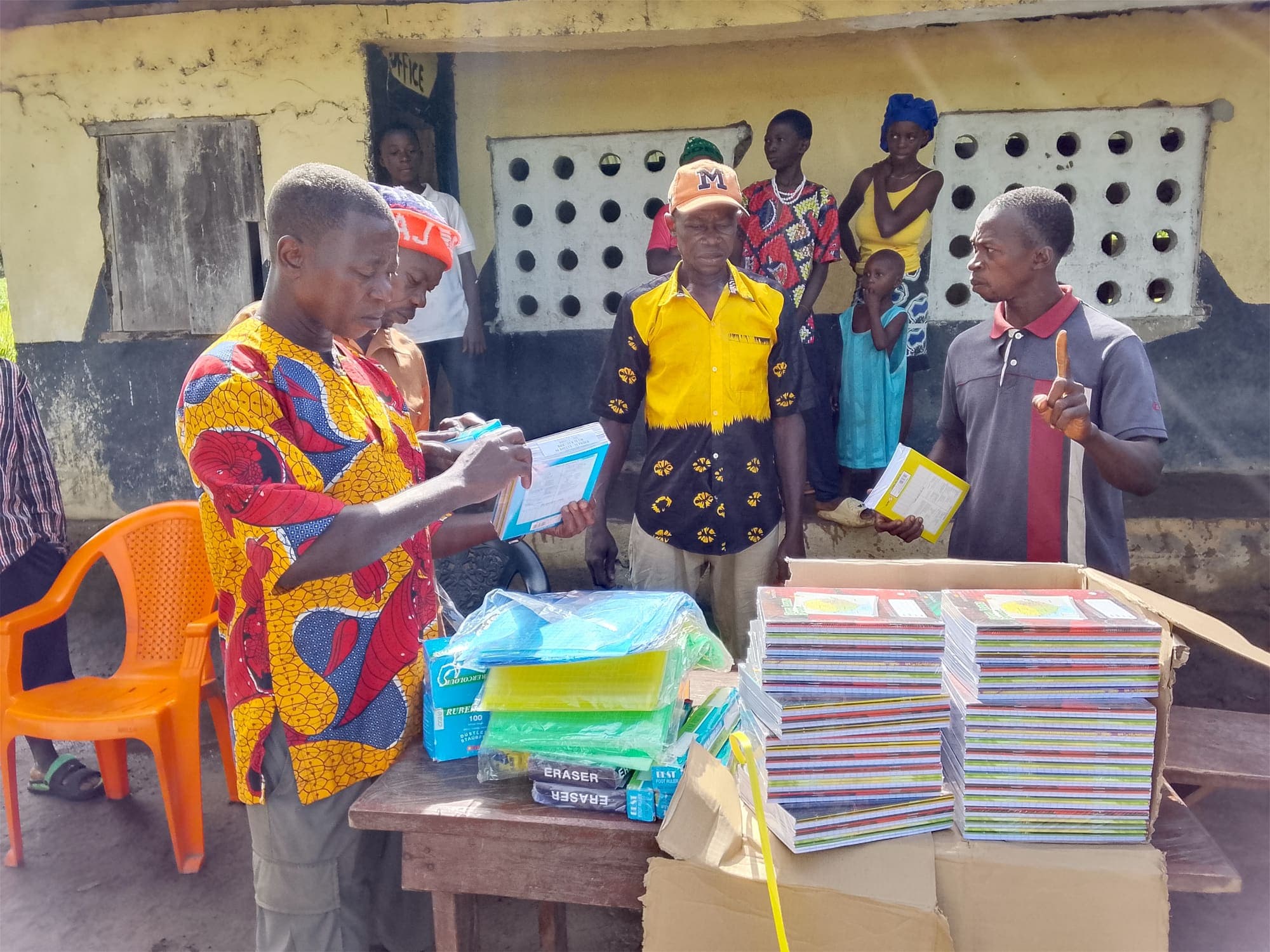 Community members sorting stacks of exercise books and school materials on a wooden table.